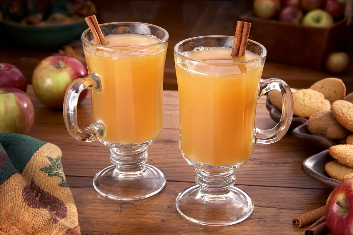 Steaming hot cider on a table with apples and ginger cookies