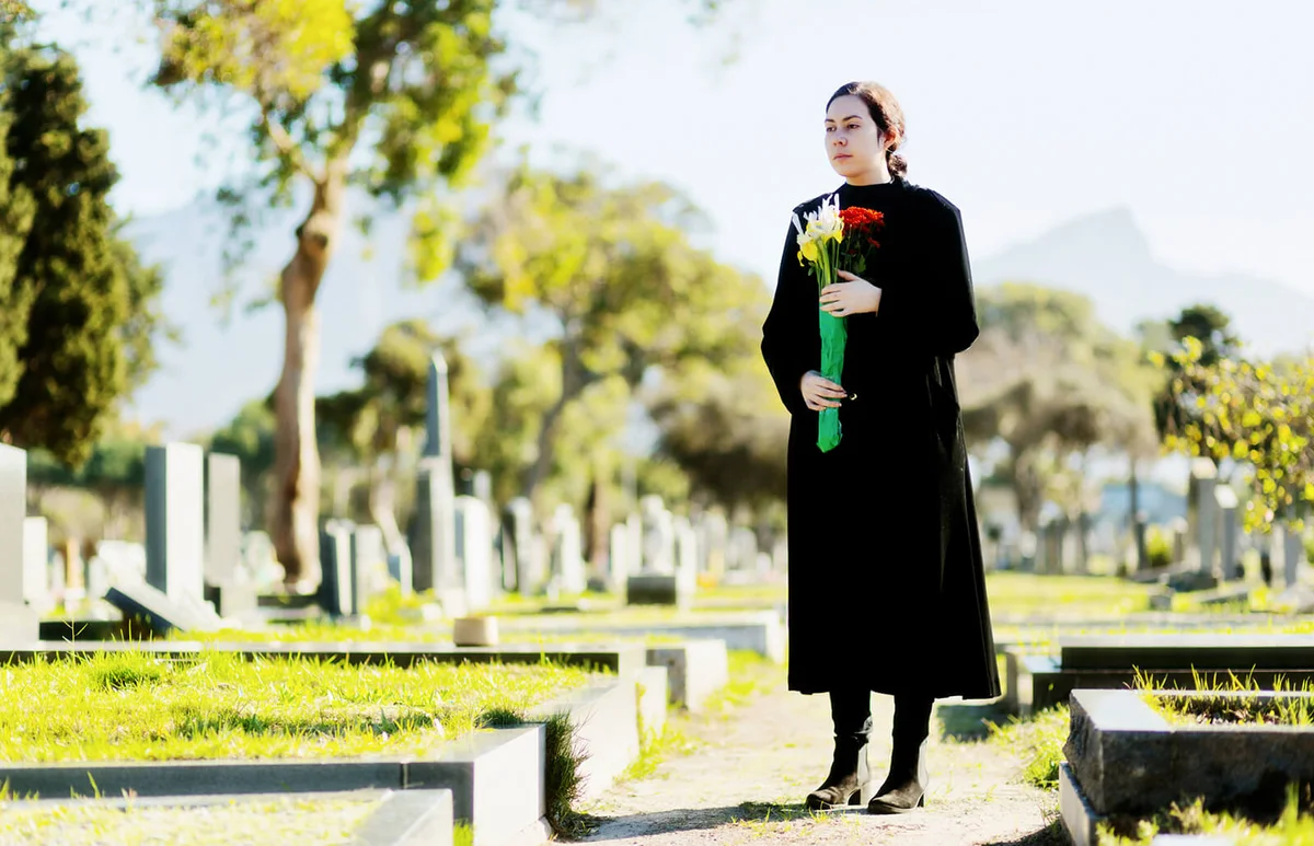 Young woman in black carrying flowers on cemetery path