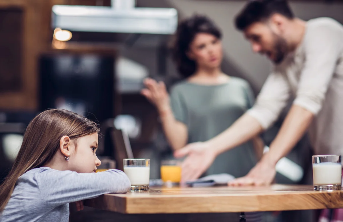 Girl feeling sad while her parents are arguing in the background