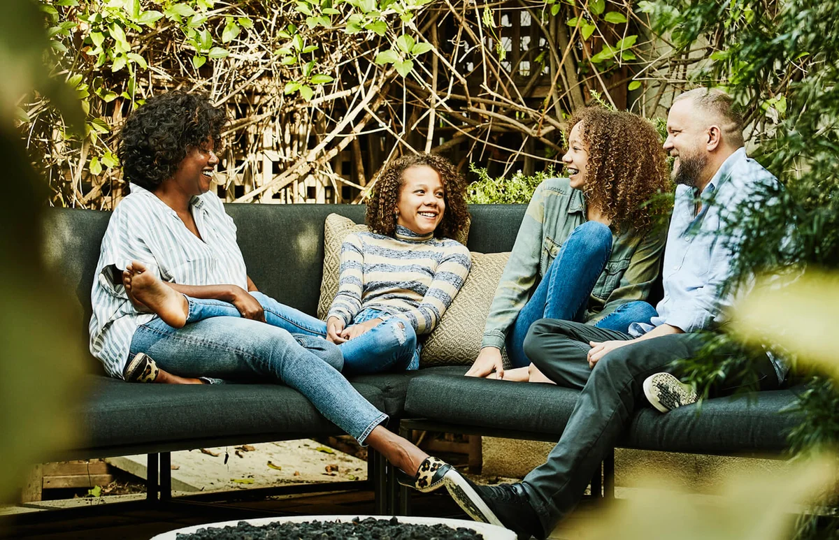 Smiling family hanging out by fire pit in backyard