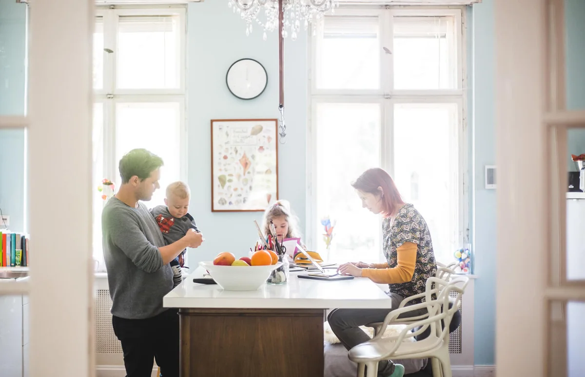 Father playing with son while standing by girl and woman busy at kitchen island