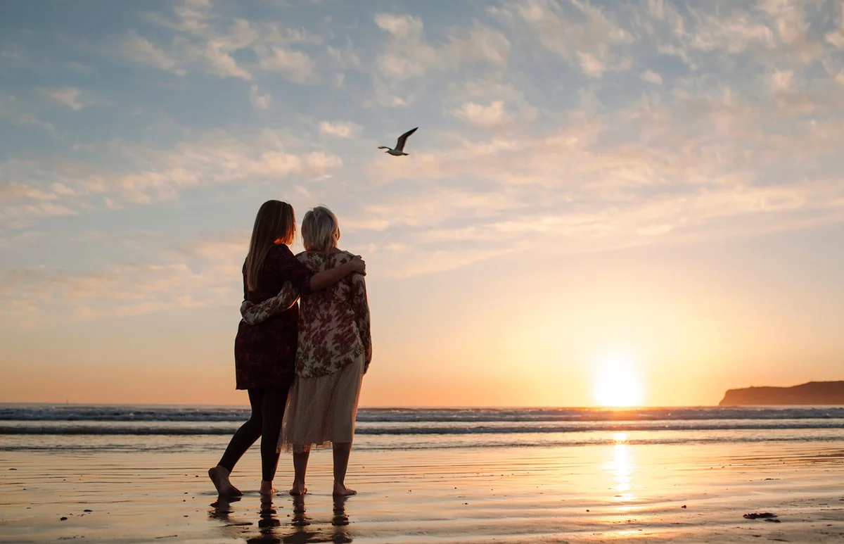 Rear view of mother and daughter looking at view while standing against sky during sunset