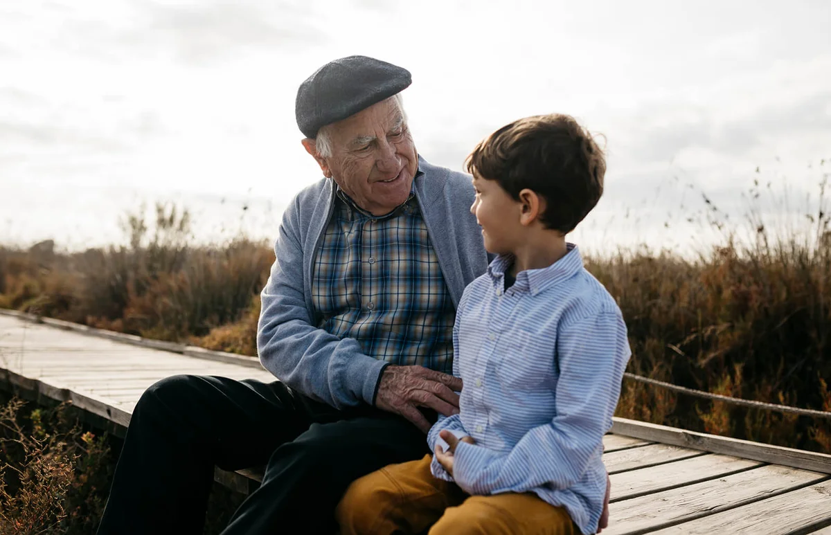 Happy grandfather sitting with his grandson on boardwalk looking at each other