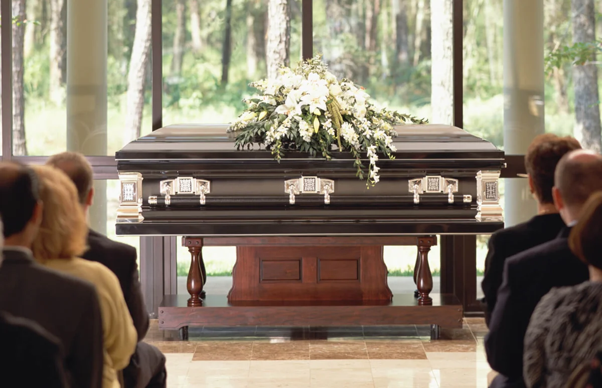 Group of people sitting at funeral, casket with flowers in front