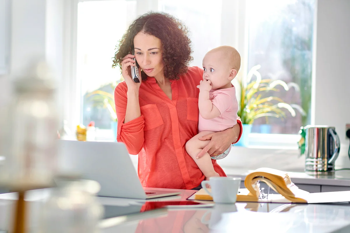 Woman in her kitchen holding a baby while talking on the phone