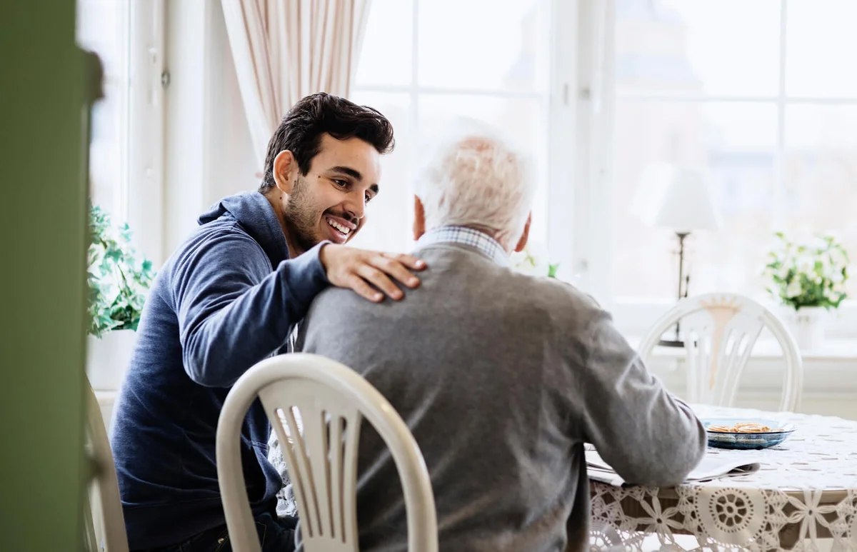 Happy caretaker communicating to senior man in nursing home