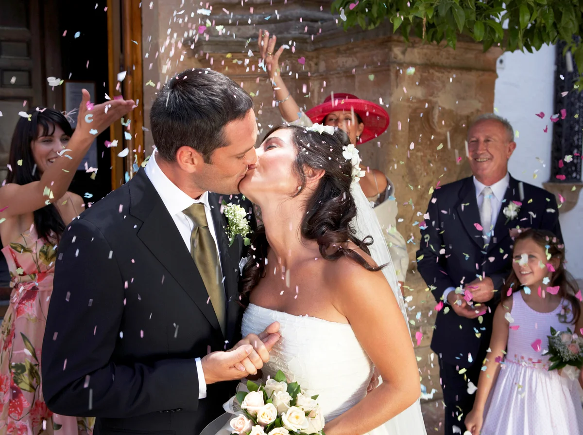 Guests throwing confetti over kissing bride and groom