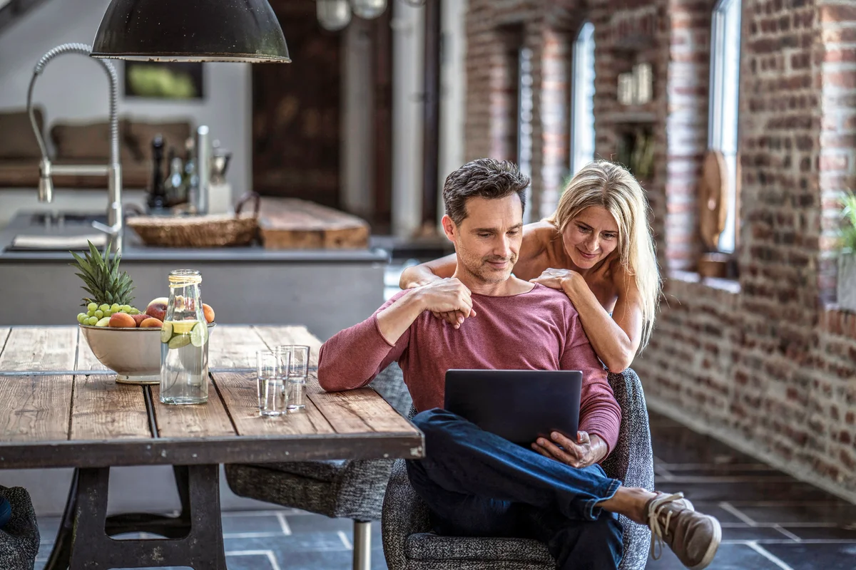 Happy couple siting in country house kitchen, looking at laptop
