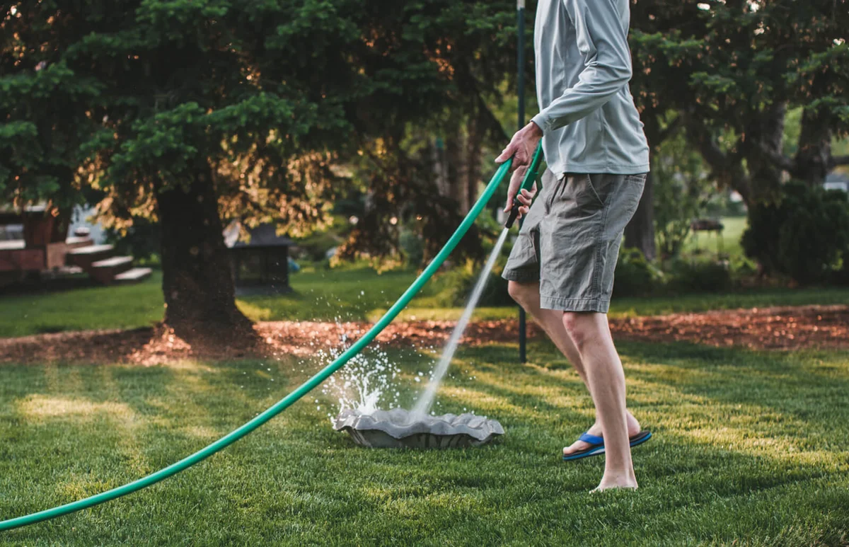 Man uses a garden hose to clean out a bird bath