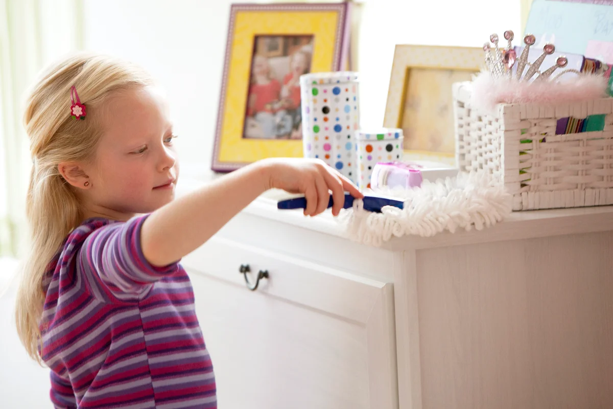 Little girl dusting dresser