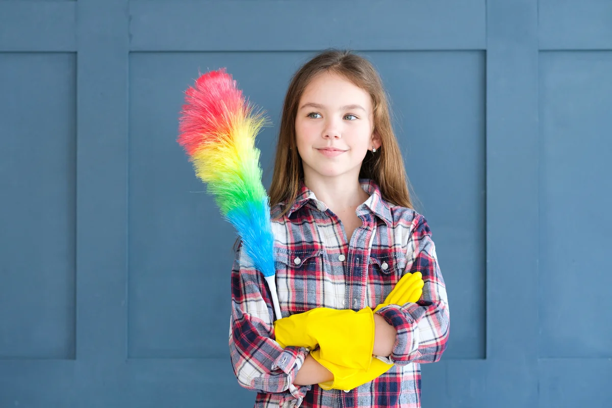 Cute girl in yellow rubber gloves and with rainbow duster