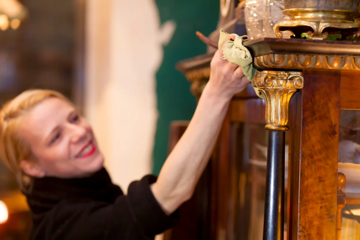 Smiling Woman Cleaning Antique Wood Cabinet
