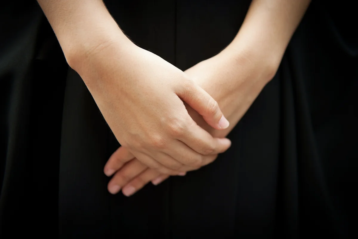 Woman wearing black respectfully folding her hands