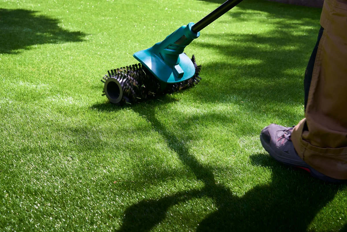 Worker uses electric brush to clean pile of fake grass