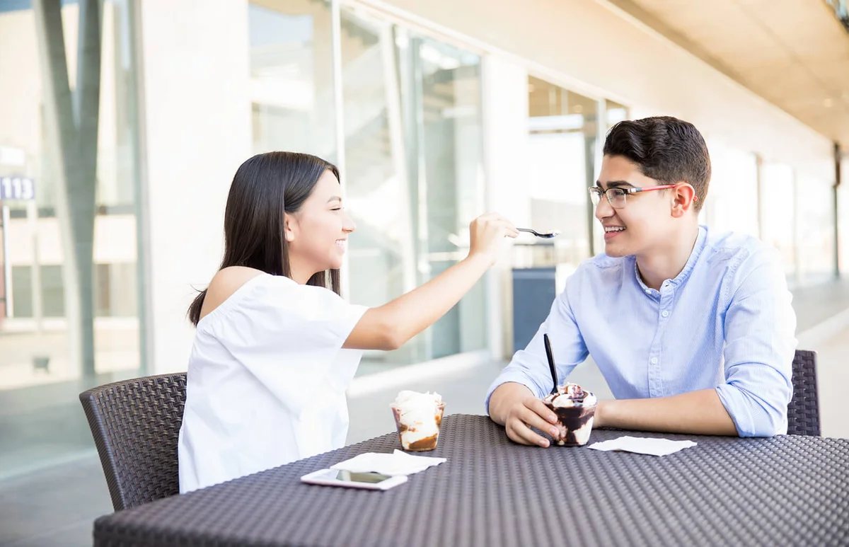 Teenage girl feeding icecream to boyfriend in cafe at shopping mall