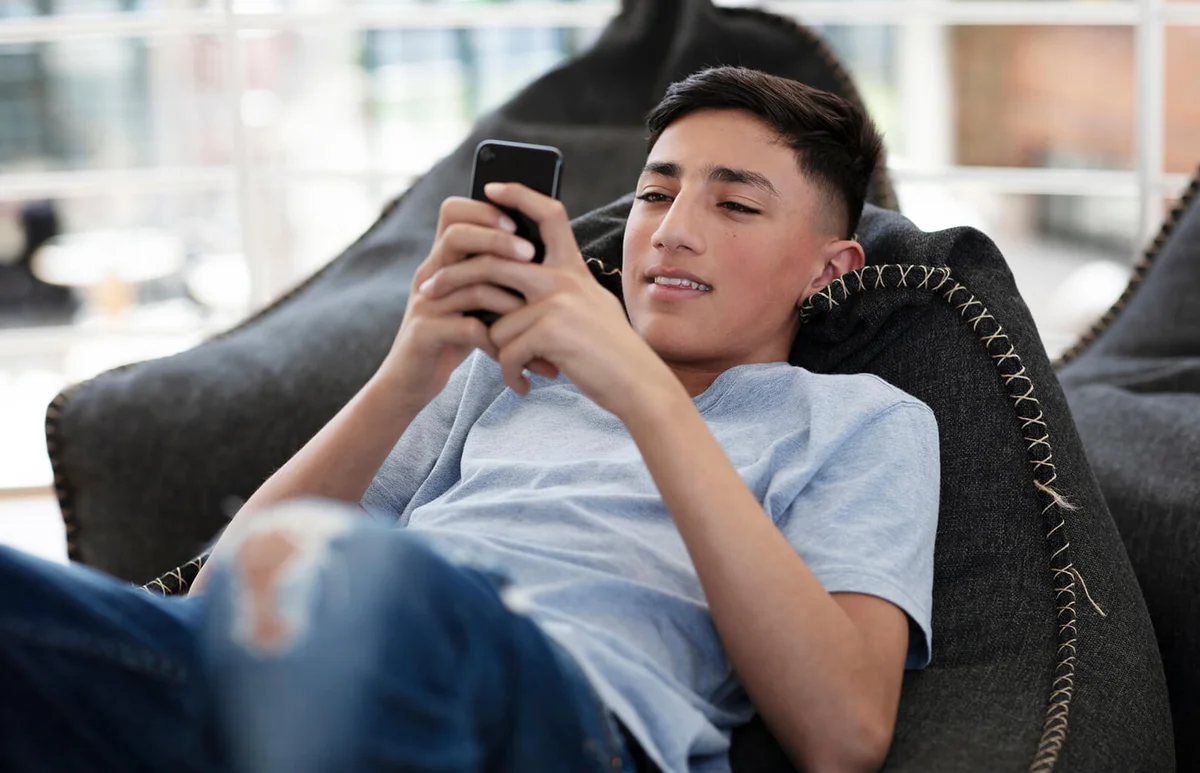 Teenage boy lying on a beanbag and reading text message on cellphone