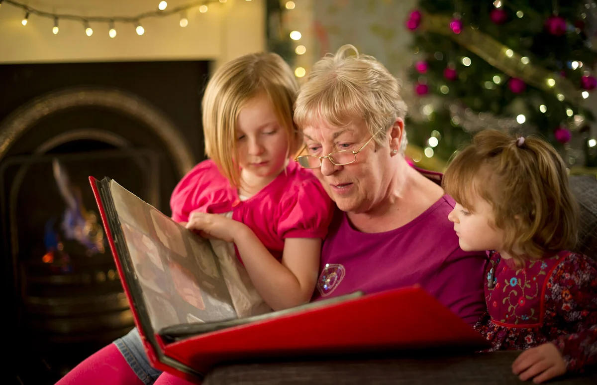 grand and granddaughters look through an old photo album
