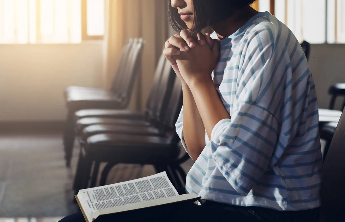 Woman praying with a bible while sitting on a chair in church
