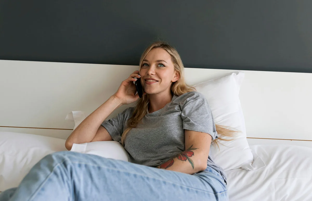Smiling young woman lying in bed talking on cell phone