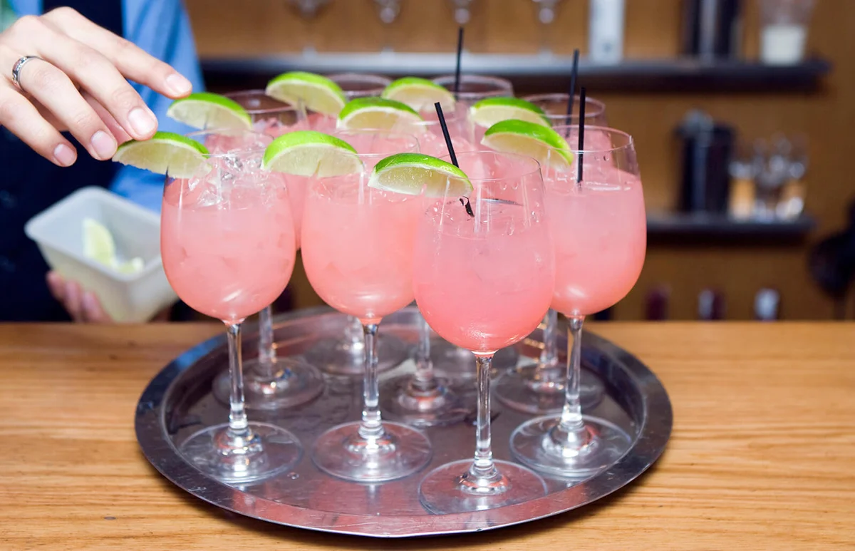 Bartender putting limes on pink cocktails