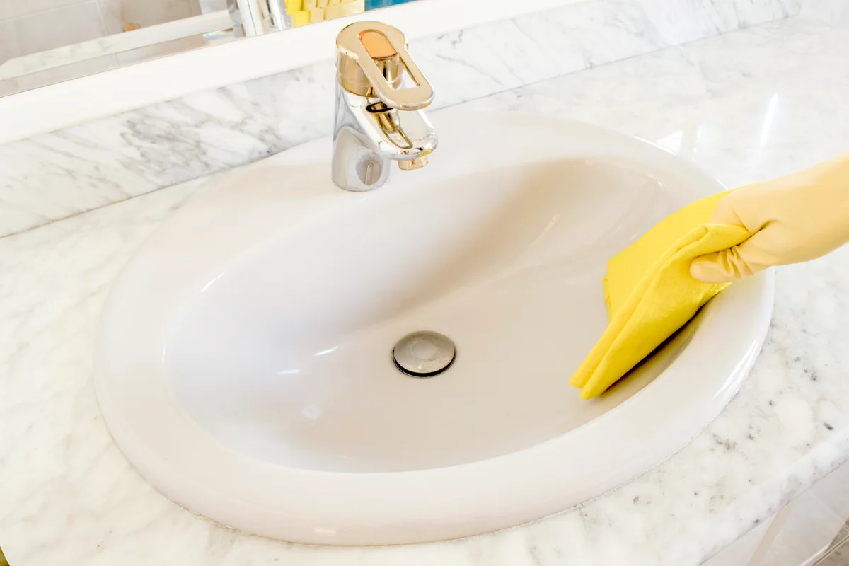 Cleaning porcelain sink with yellow gloves