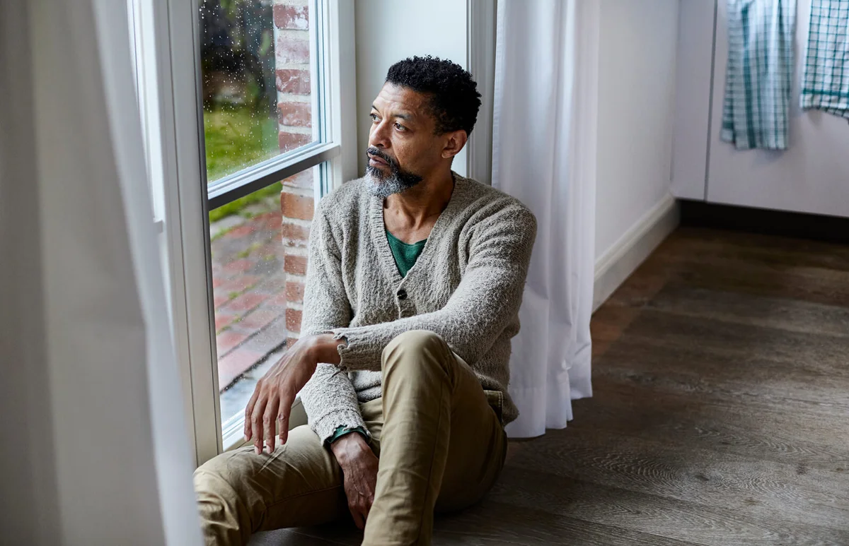 Pensive man sitting on the floor looking out of window