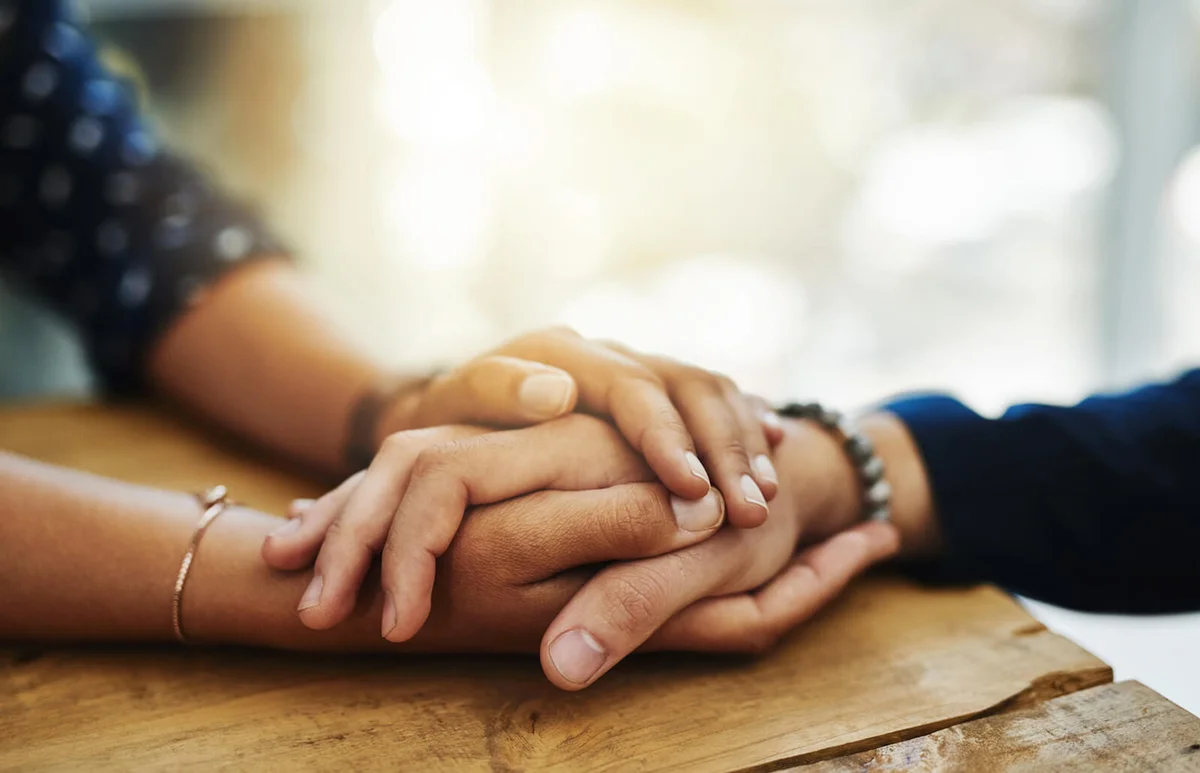 two unrecognizable people holding hands in comfort