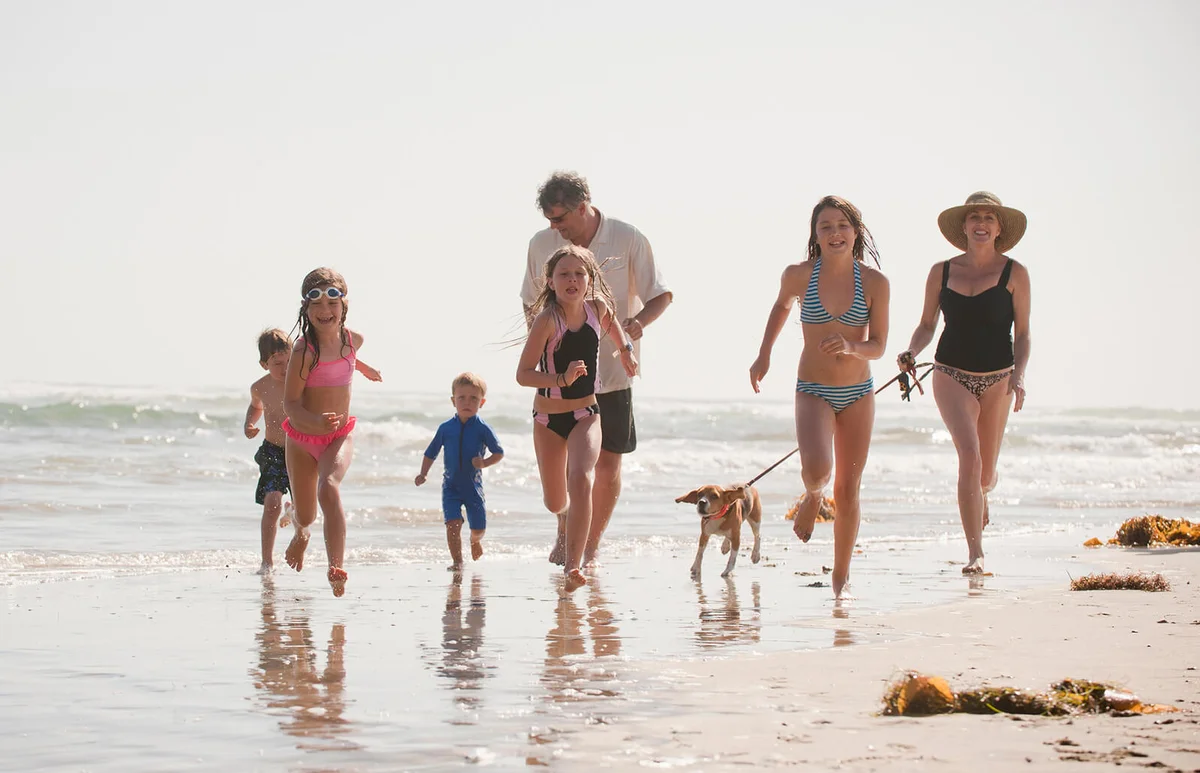 family of seven runs on the beach with their dog