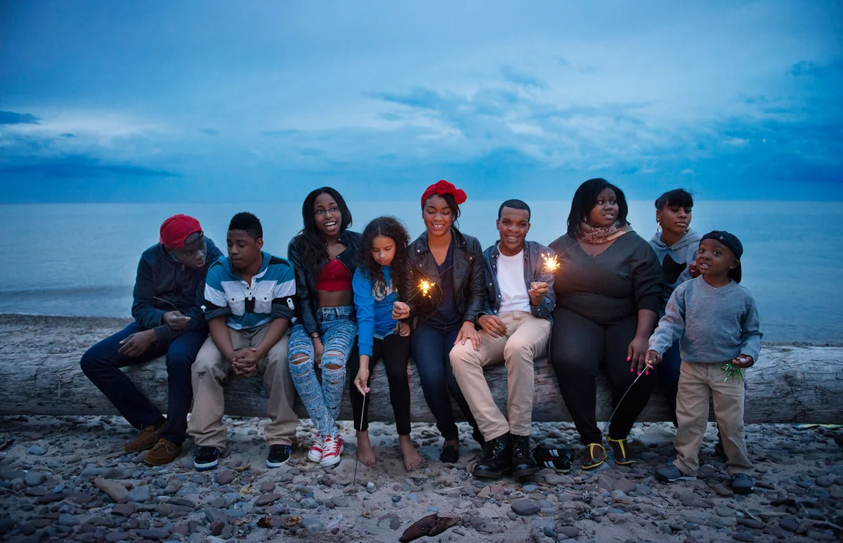 Family and friends sitting on log at beach against sky