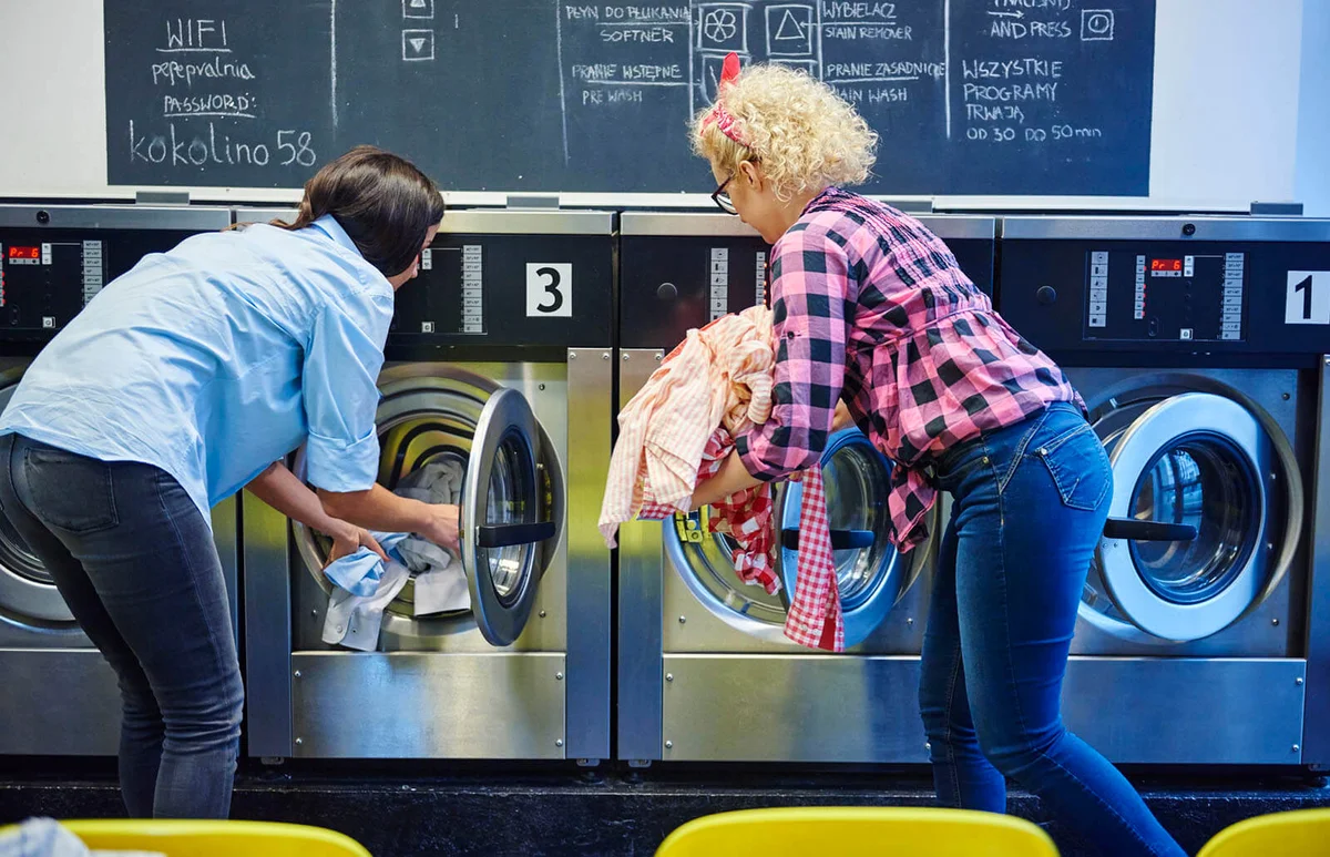 women inserting laundry into washing machines at laundrette