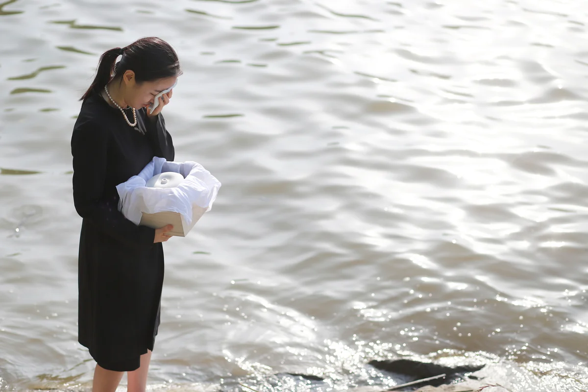woman with cremated ashes in urn standing by river