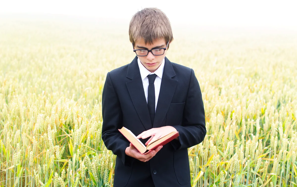 boy reading poem from book in field