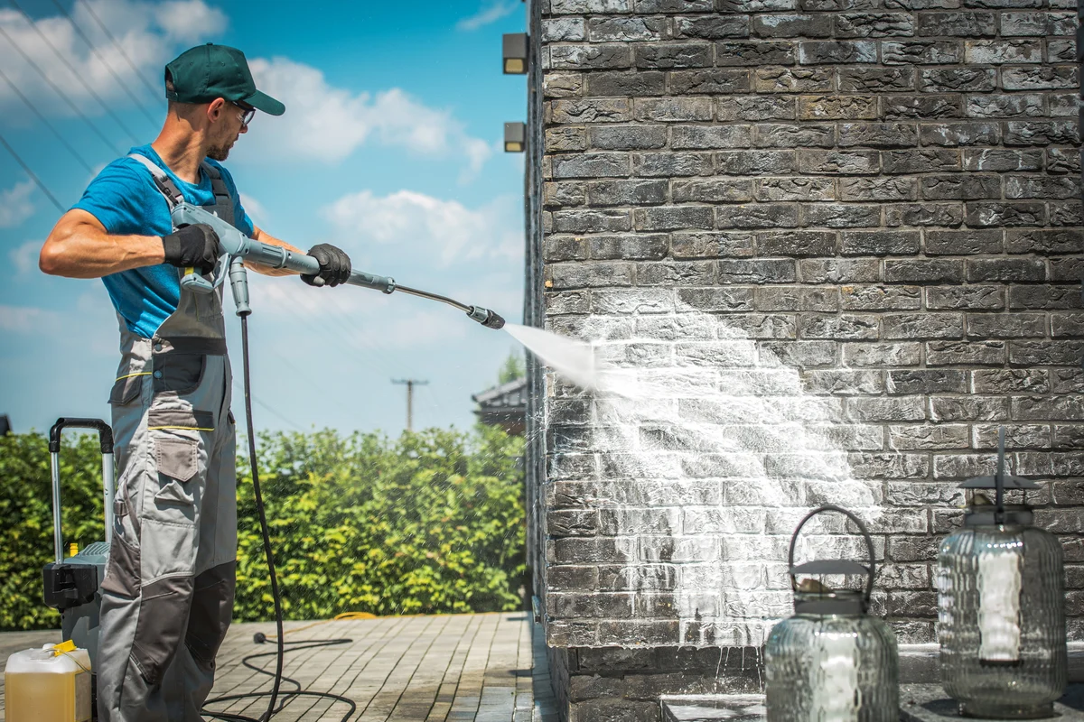 man using pressure washer to clean exterior brick wall