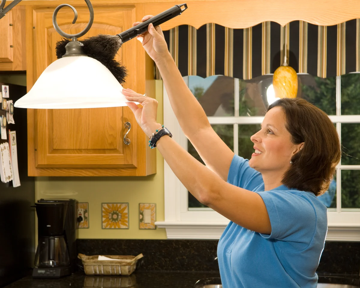 woman using duster to dust kitchen lamp ahdes