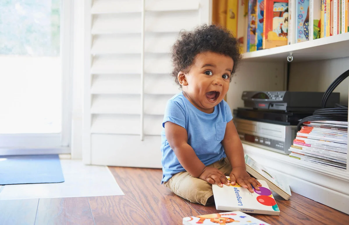 Surprised baby boy sitting on floor playing with books