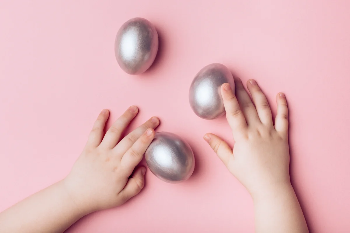 Children's hands and silver eggs on a pink background