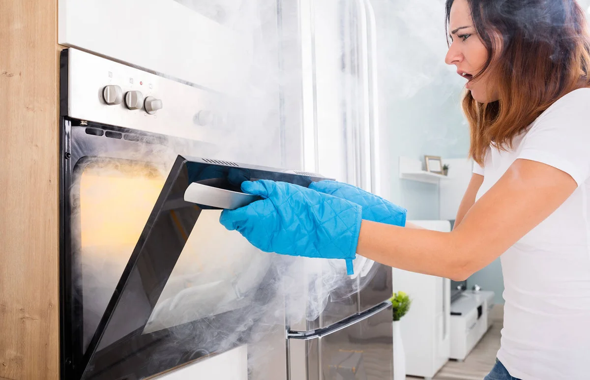 Woman Opening Door Of Oven Full Of Smoke