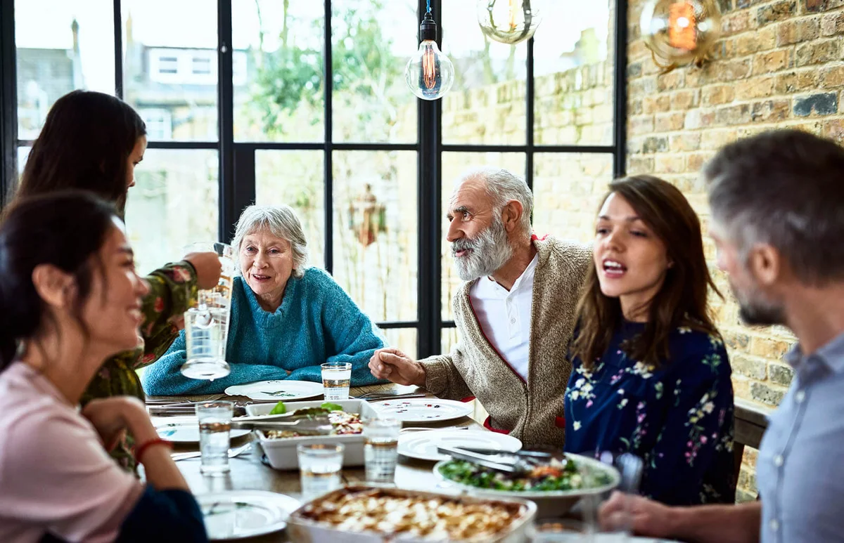 Extended family sitting round dinner table chatting and eating dinner