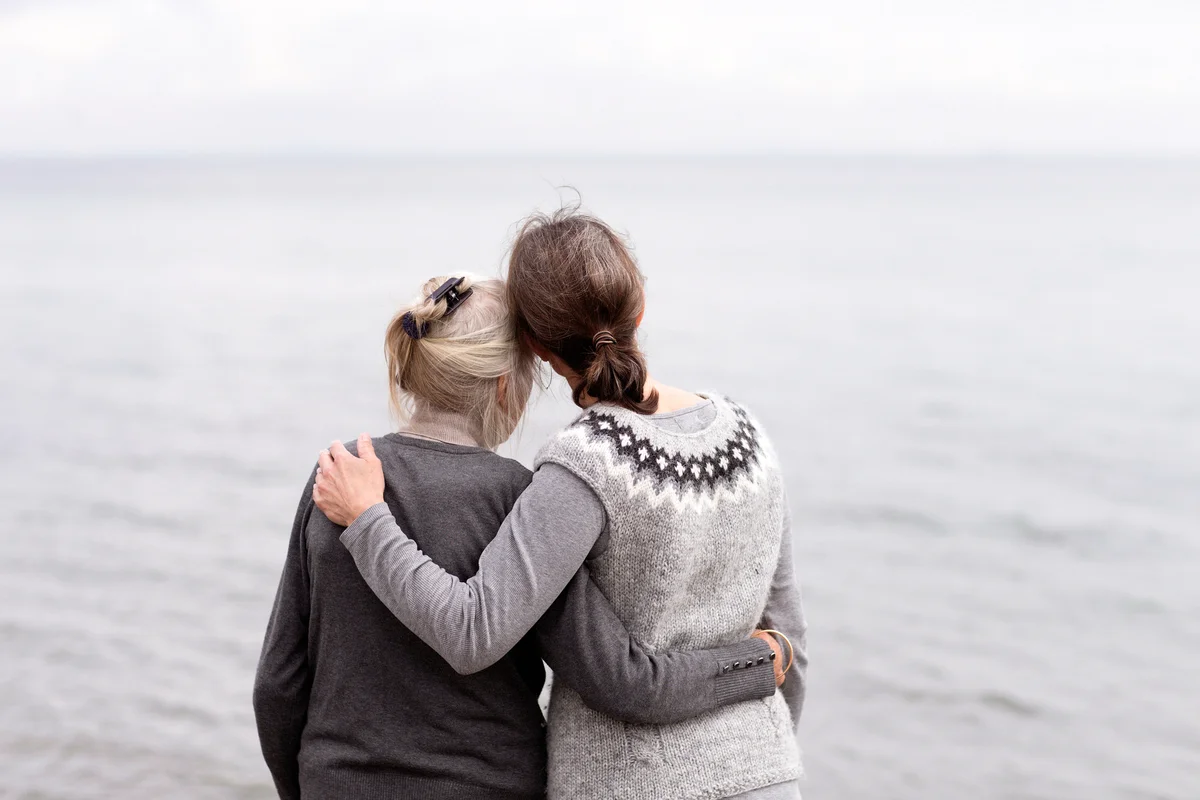 Two generations women embracing, looking at sea