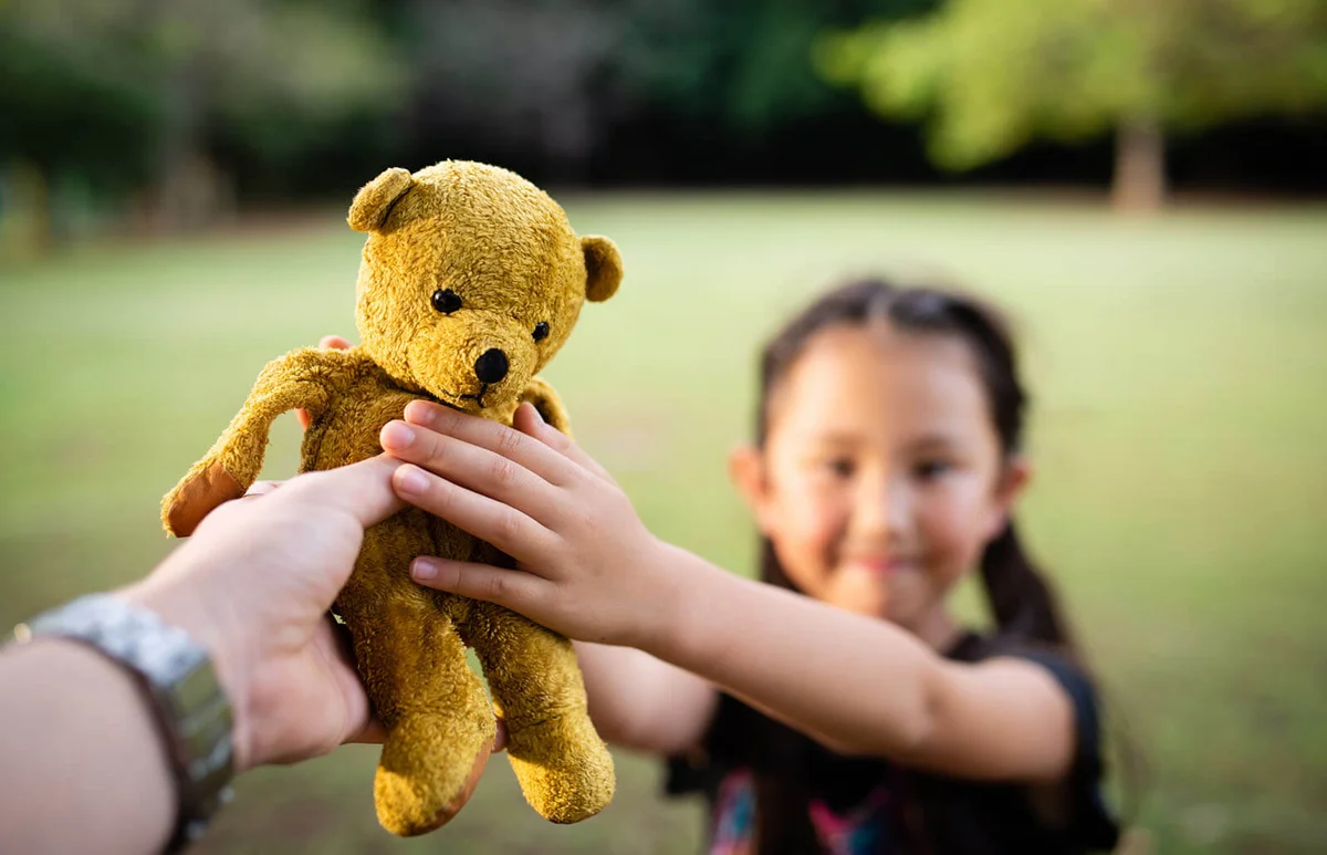Parent and child handing teddy bear