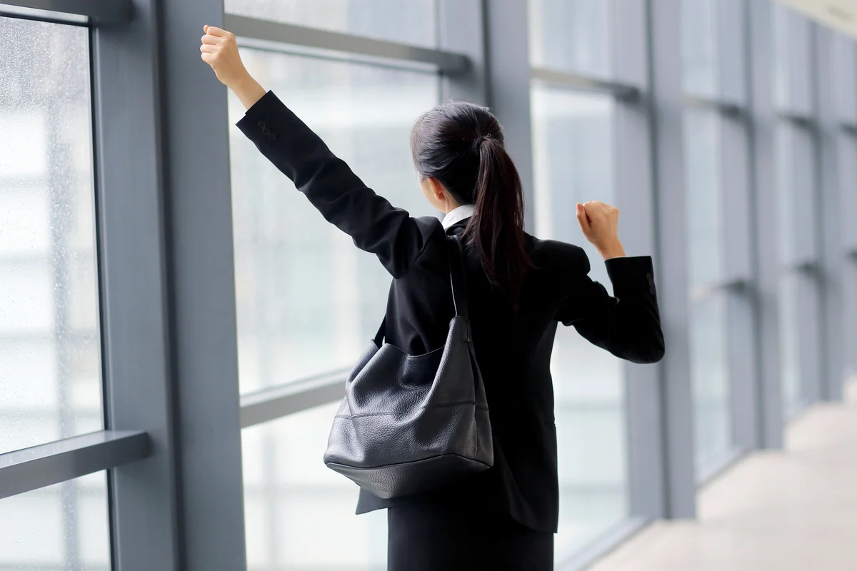 Businesswoman with arms raised in corridor while caring a charcoal purse