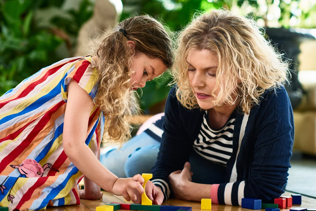 Young girl concentrating on building blocks with her mother and talking