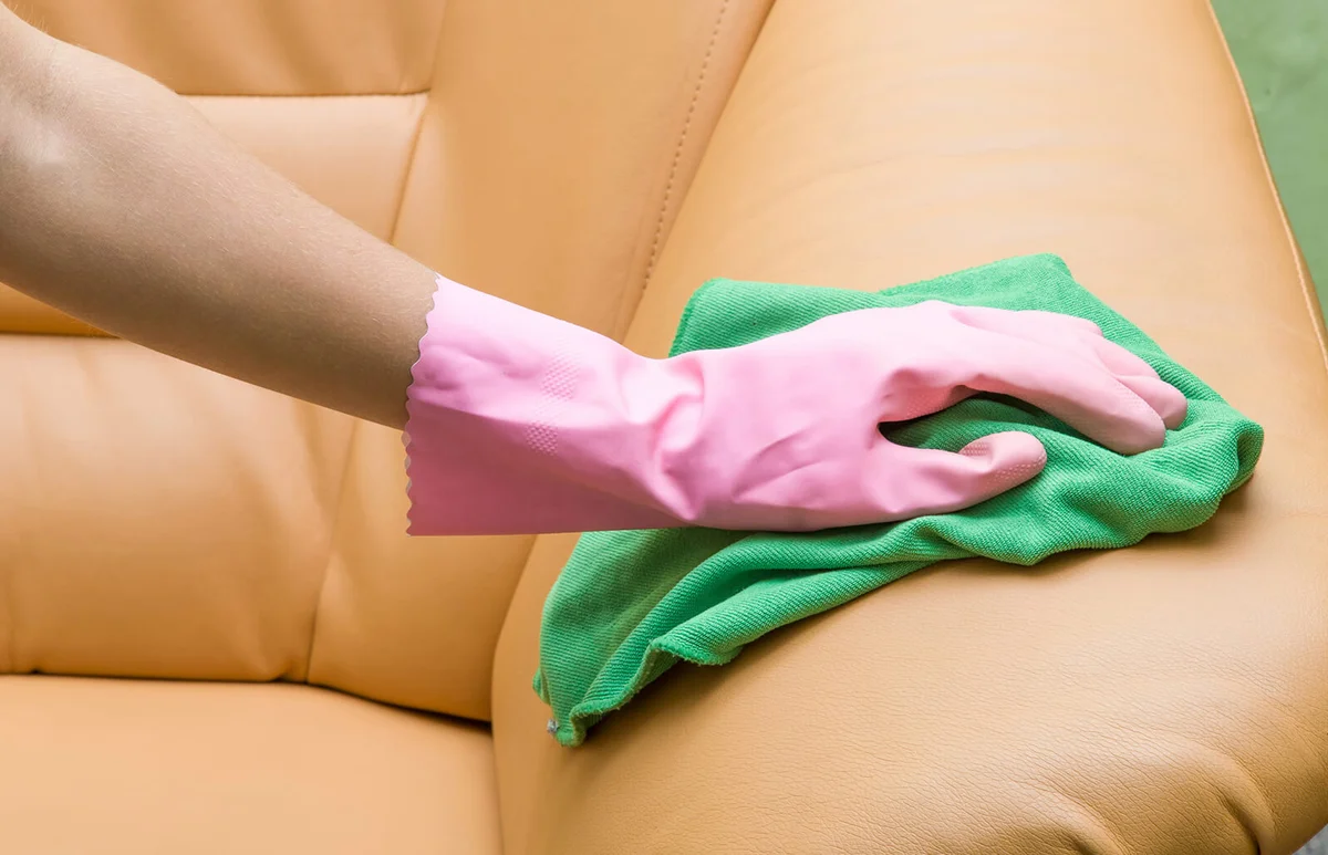 Hand in pink protective glove wiping leather sofa with cloth