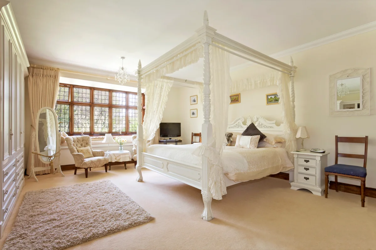 White four-poster bed in large neutral-colored bedroom