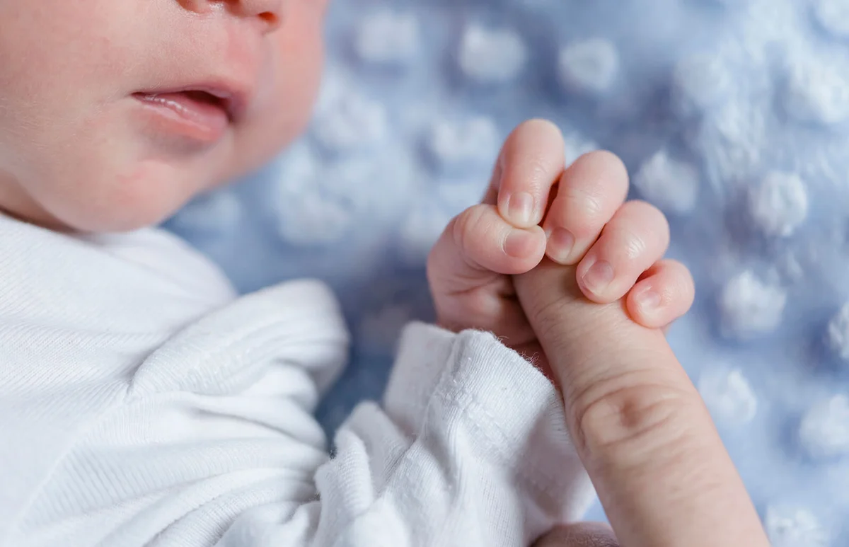 Newborn baby boy holding finger