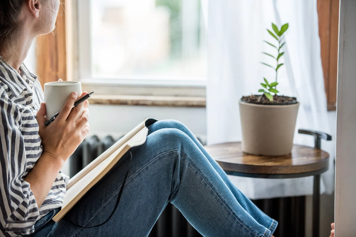 A young woman writing on her journal close to a window