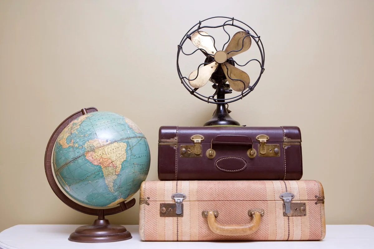 Retro items including two suitcases, a globe and a fan that sit on a white table