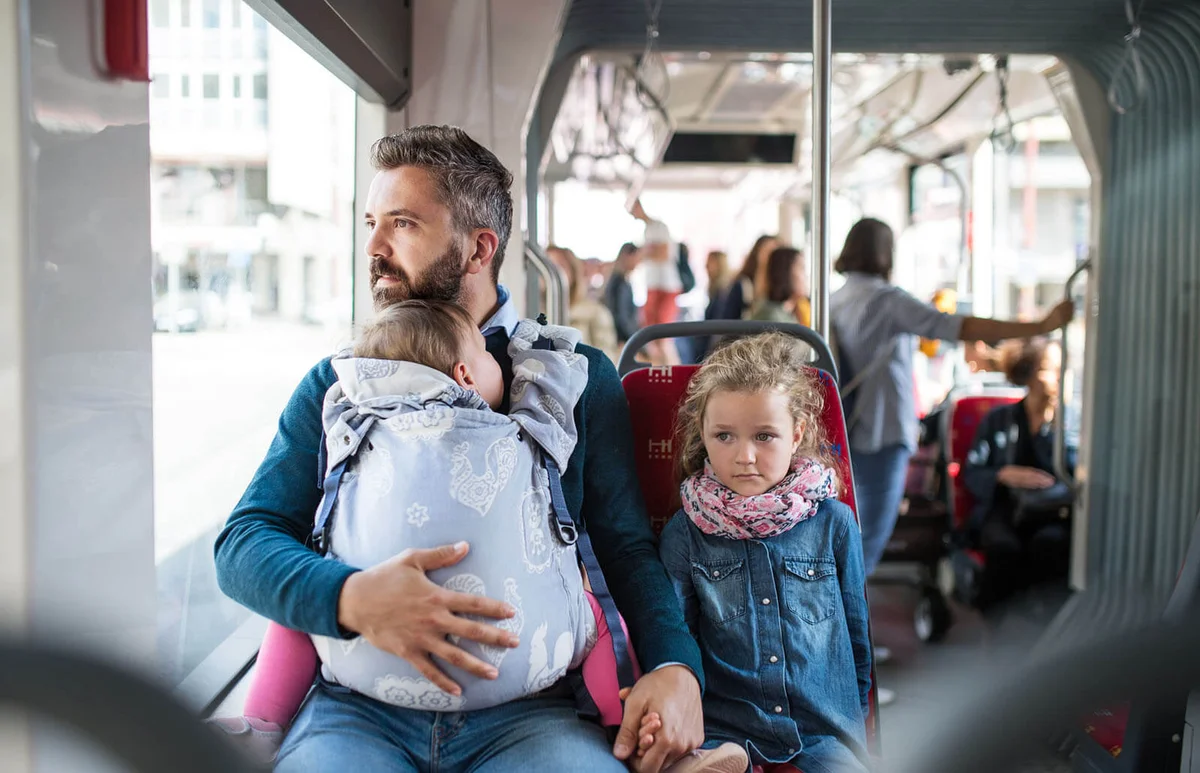 Father with daughter and toddler in carrier sitting on bus in city