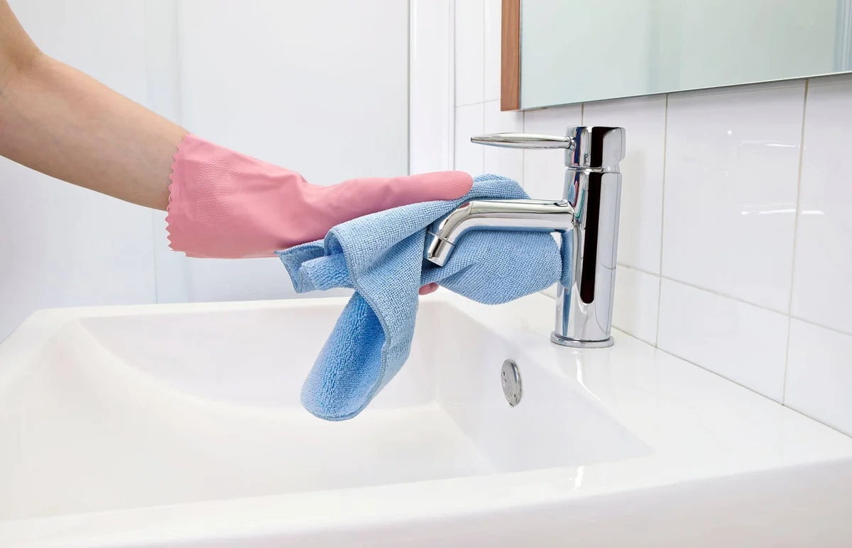 woman cleaning the faucet with microfiber cloth and gloves