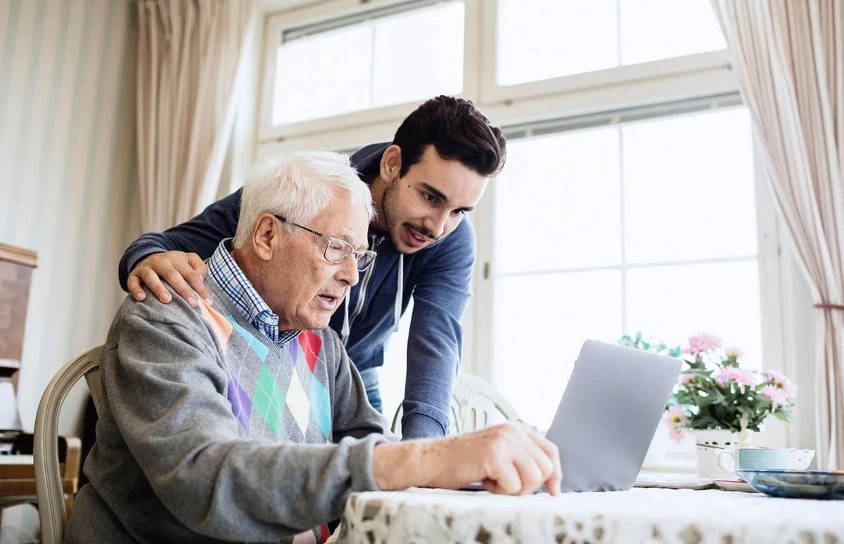 Caretaker and senior man using laptop in nursing home